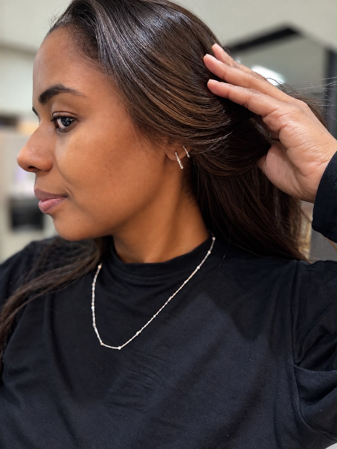 Mulher com gargantilha prateada delicada e brinco ear cuff cravejado, blusa preta